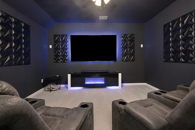 carpeted cinema room with a warm lit fireplace, a ceiling fan, visible vents, and baseboards