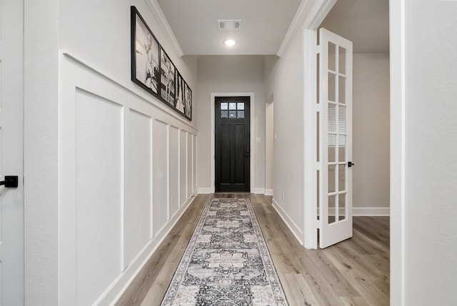 doorway featuring light wood-style flooring, visible vents, baseboards, and crown molding