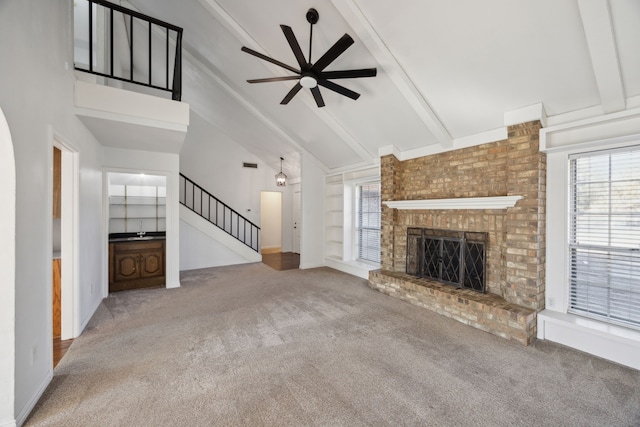 unfurnished living room featuring stairway, carpet, a brick fireplace, built in shelves, and beam ceiling