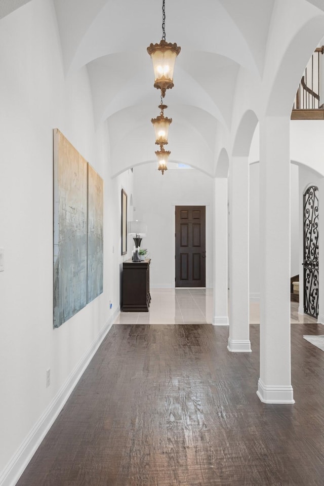 foyer entrance featuring decorative columns, vaulted ceiling, baseboards, and wood finished floors