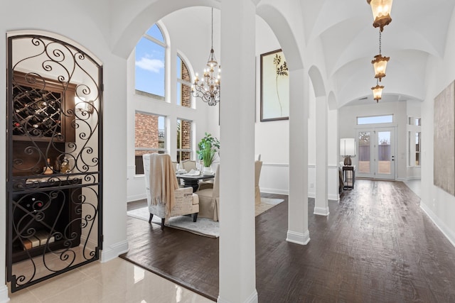 foyer entrance featuring a healthy amount of sunlight, a towering ceiling, a notable chandelier, and wood finished floors