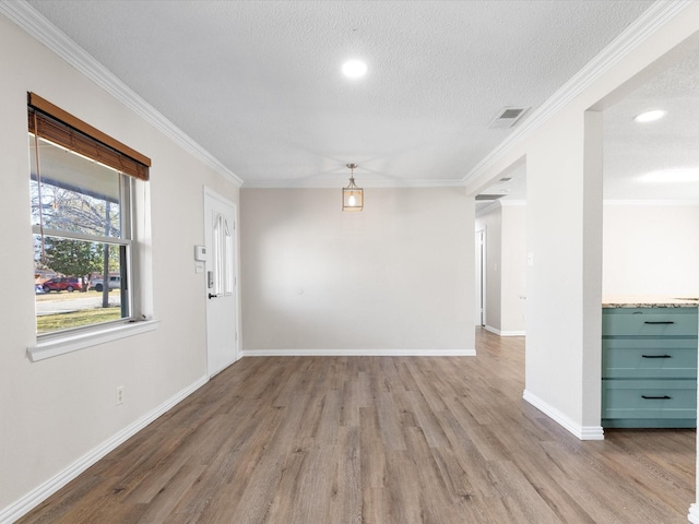 spare room with a textured ceiling, ornamental molding, visible vents, and light wood-style floors