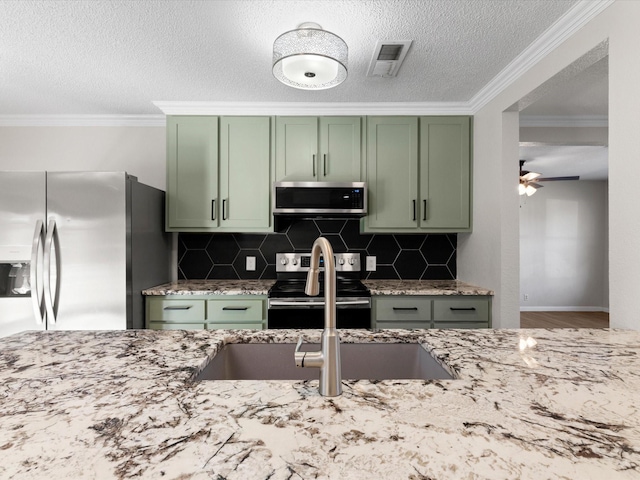 kitchen featuring green cabinets, appliances with stainless steel finishes, ornamental molding, and light stone countertops