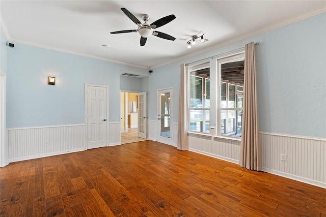 empty room featuring hardwood / wood-style flooring, ceiling fan, crown molding, and wainscoting