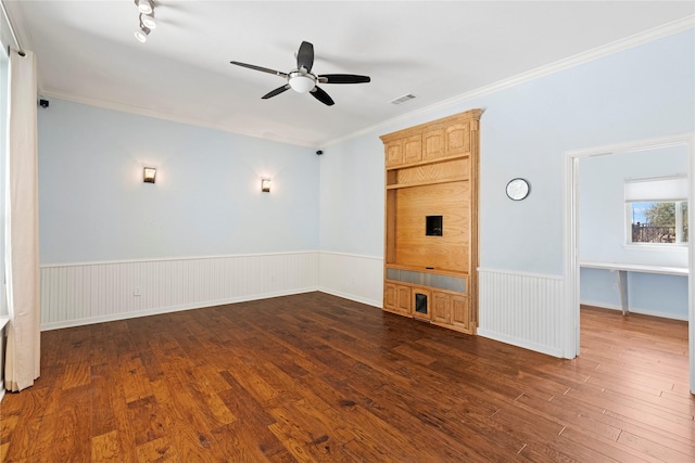 unfurnished living room with dark wood-type flooring, wainscoting, crown molding, and ceiling fan