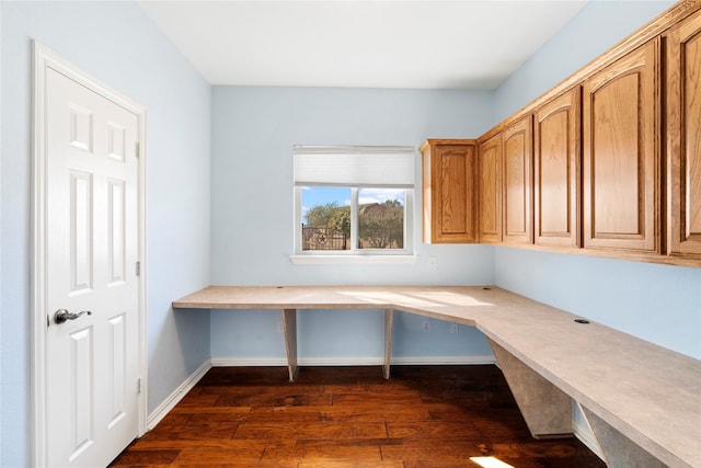 unfurnished office featuring dark wood-type flooring, built in desk, and baseboards