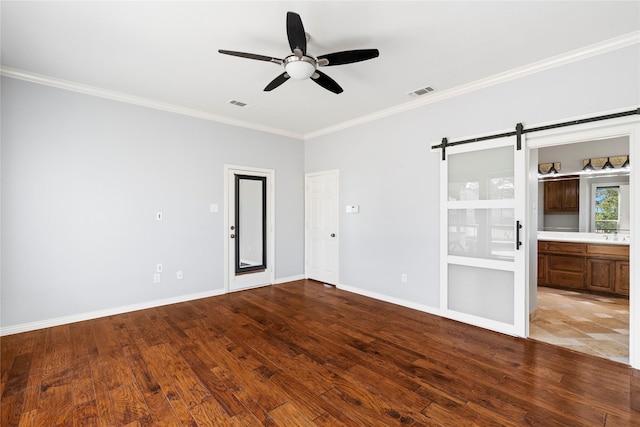 spare room featuring light wood-style floors, crown molding, baseboards, and a barn door