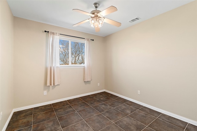 spare room featuring a ceiling fan, dark tile patterned flooring, visible vents, and baseboards