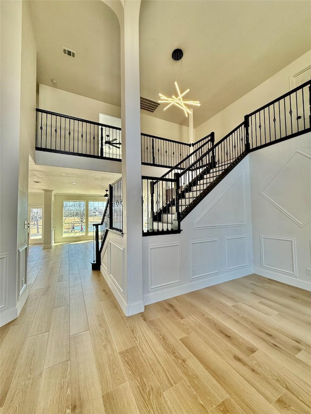 stairs featuring visible vents, a towering ceiling, wood finished floors, a chandelier, and a decorative wall