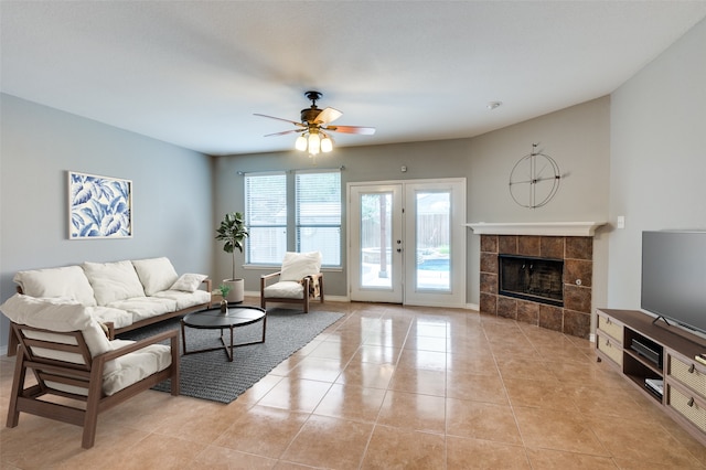 living area featuring light tile patterned flooring, a tile fireplace, a ceiling fan, baseboards, and french doors