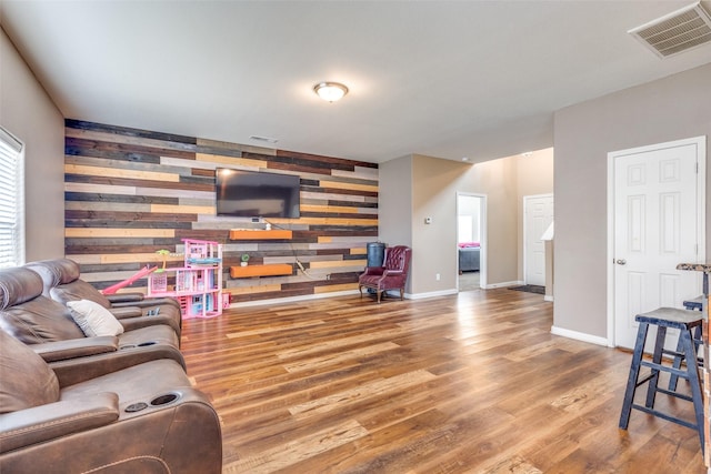 living area featuring visible vents, an accent wall, wooden walls, wood finished floors, and baseboards