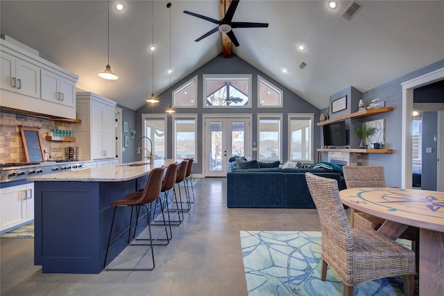 kitchen featuring a breakfast bar, white cabinetry, light stone countertops, an island with sink, and pendant lighting