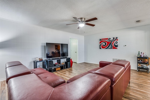 living area with a ceiling fan, a textured ceiling, visible vents, and wood finished floors