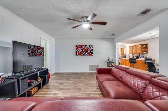 living room featuring a textured ceiling, light wood-type flooring, visible vents, and a ceiling fan