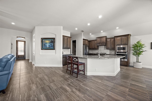 kitchen with arched walkways, a center island with sink, stainless steel appliances, open floor plan, and under cabinet range hood