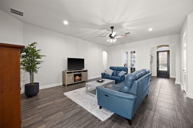 living room with a warm lit fireplace, baseboards, visible vents, and arched walkways