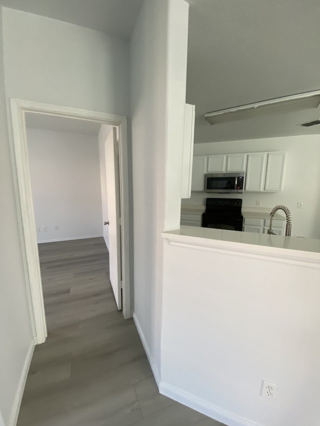 hallway with visible vents, baseboards, a sink, and wood finished floors