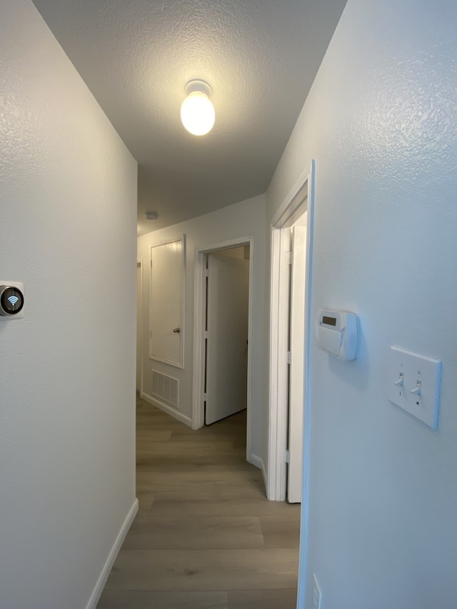 hall featuring baseboards, a textured ceiling, visible vents, and wood finished floors