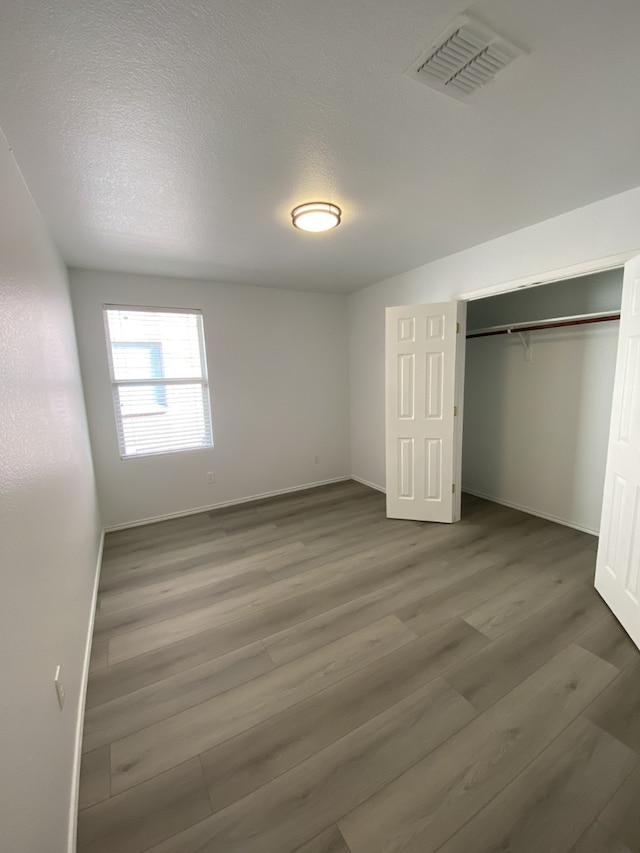 unfurnished bedroom with a textured ceiling, wood finished floors, visible vents, and baseboards