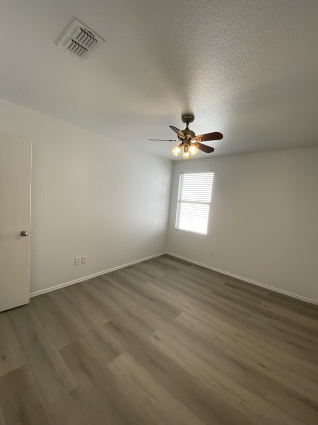 unfurnished room featuring baseboards, visible vents, dark wood finished floors, ceiling fan, and a textured ceiling