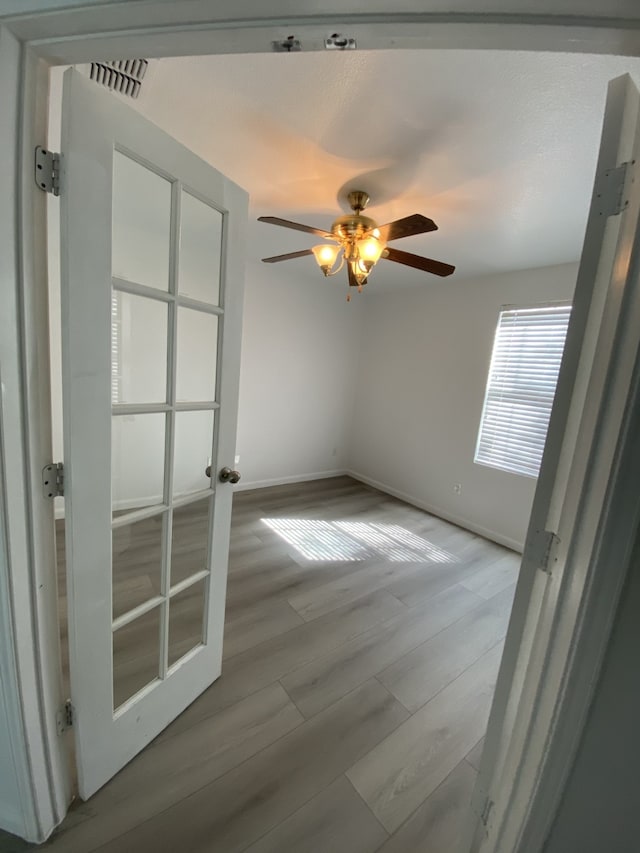 empty room with ceiling fan, wood finished floors, visible vents, and baseboards