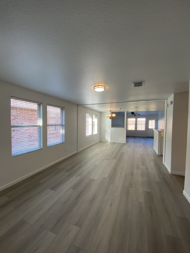 unfurnished living room featuring a chandelier, a textured ceiling, wood finished floors, visible vents, and baseboards