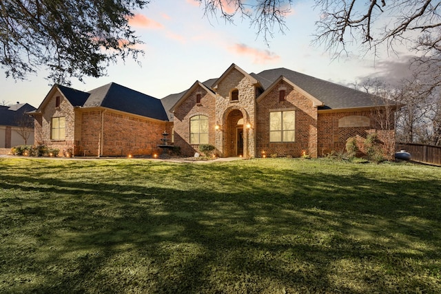 french country style house featuring brick siding, fence, a front lawn, and roof with shingles