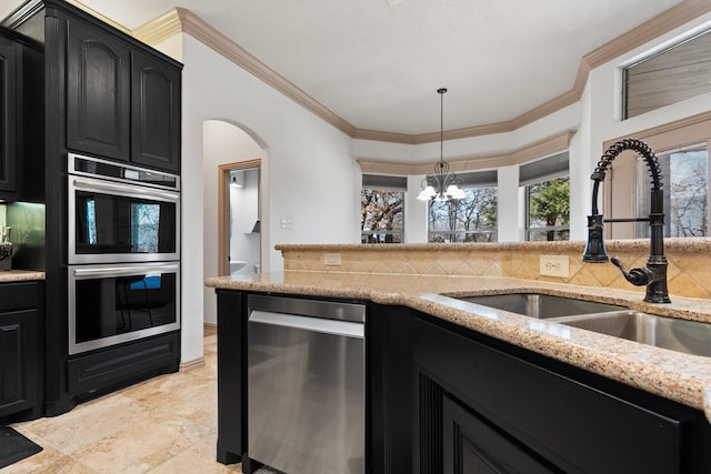 kitchen with stainless steel appliances, a sink, dark cabinetry, light stone countertops, and tasteful backsplash