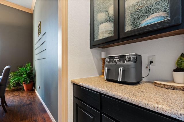 interior space featuring baseboards, light stone countertops, dark wood-style floors, glass insert cabinets, and crown molding