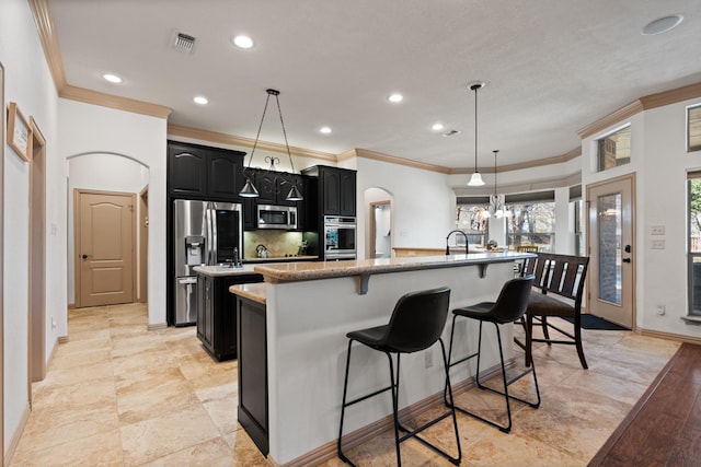 kitchen with a kitchen breakfast bar, dark cabinets, a kitchen island with sink, stainless steel appliances, and backsplash