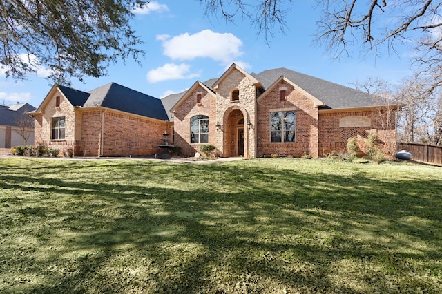 view of front facade with brick siding, a shingled roof, fence, stone siding, and a front lawn