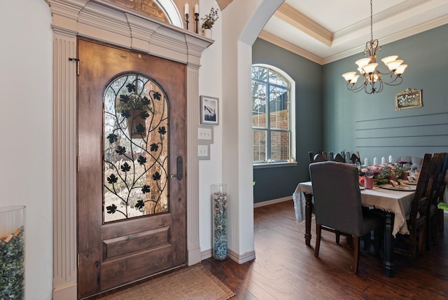 entryway with arched walkways, dark wood-style flooring, ornamental molding, a raised ceiling, and an inviting chandelier