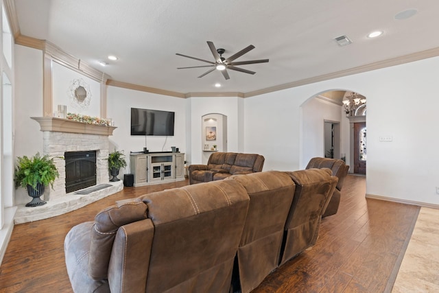 living room with ceiling fan, a fireplace, wood finished floors, visible vents, and ornamental molding