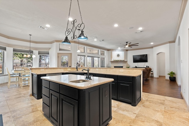 kitchen with visible vents, arched walkways, ornamental molding, dark cabinets, and a kitchen island with sink