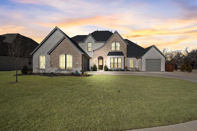 french country style house with a garage, brick siding, a yard, and driveway