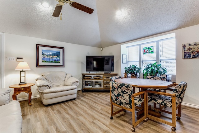 dining area featuring lofted ceiling, light wood-style floors, a ceiling fan, a textured ceiling, and baseboards