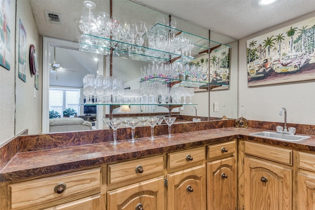 interior space featuring indoor wet bar, visible vents, a ceiling fan, a sink, and a textured ceiling