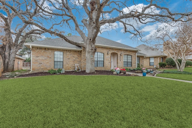 view of front facade featuring a front lawn, a shingled roof, and brick siding