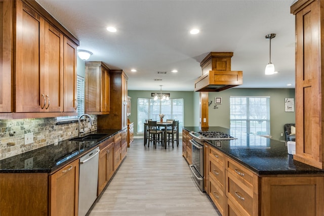 kitchen with a sink, appliances with stainless steel finishes, dark stone counters, brown cabinetry, and pendant lighting