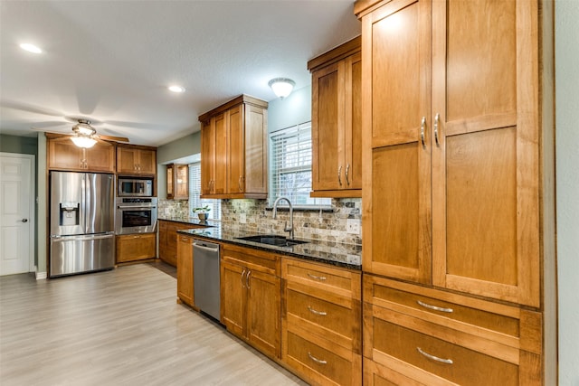 kitchen featuring stainless steel appliances, dark stone counters, brown cabinets, and a sink