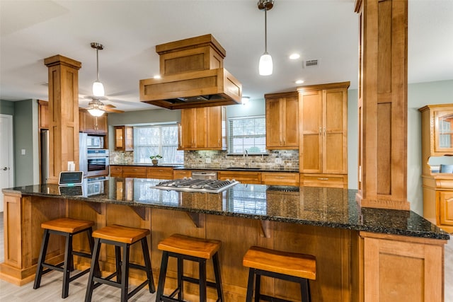 kitchen featuring a sink, appliances with stainless steel finishes, tasteful backsplash, dark stone countertops, and ornate columns