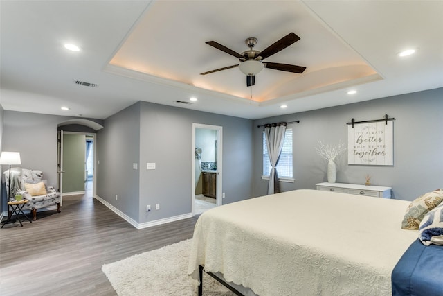 bedroom with baseboards, visible vents, arched walkways, wood finished floors, and a tray ceiling