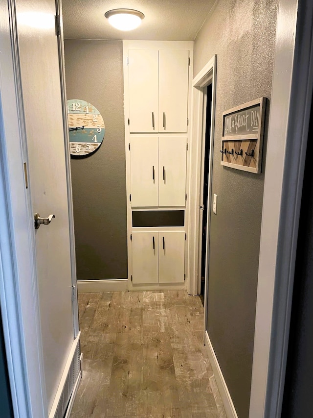 hallway featuring a textured ceiling, baseboards, wood finished floors, and a textured wall