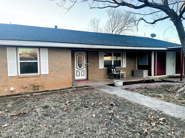 view of front of home featuring roof with shingles, a porch, and brick siding