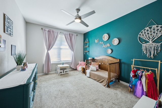 carpeted bedroom with an accent wall, ceiling fan, and baseboards