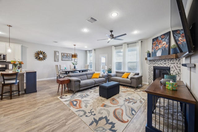 living room featuring light wood-style flooring, recessed lighting, visible vents, baseboards, and a glass covered fireplace