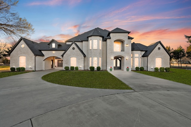 french country home featuring a yard, a shingled roof, and curved driveway