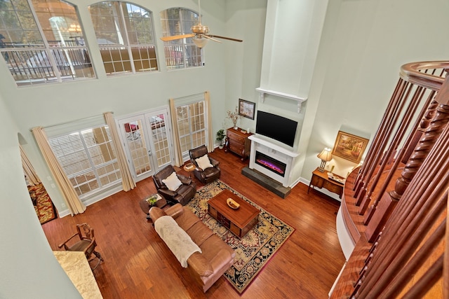 living room with french doors, a high ceiling, wood finished floors, and a glass covered fireplace