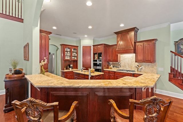 kitchen featuring a peninsula, appliances with stainless steel finishes, custom exhaust hood, dark wood-style floors, and tasteful backsplash