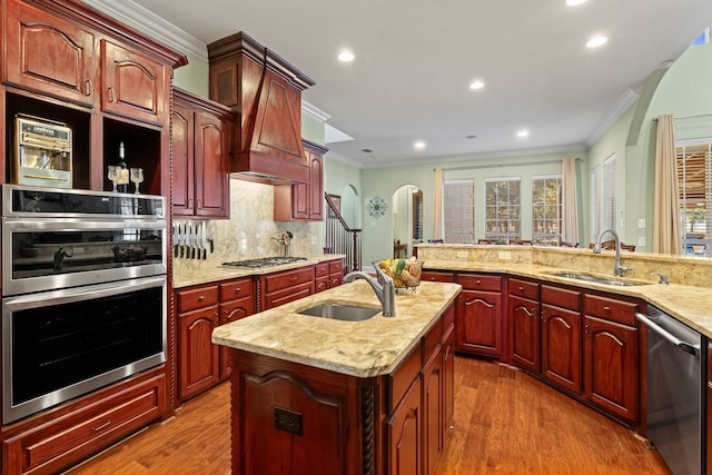 kitchen featuring stainless steel appliances, a kitchen island with sink, a sink, and wood finished floors